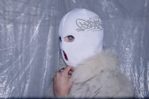 Person in balaclava with graffiti motif, one eye visible, faux fur detail, against tarp background, edgy design asset for modern mockup graphics.